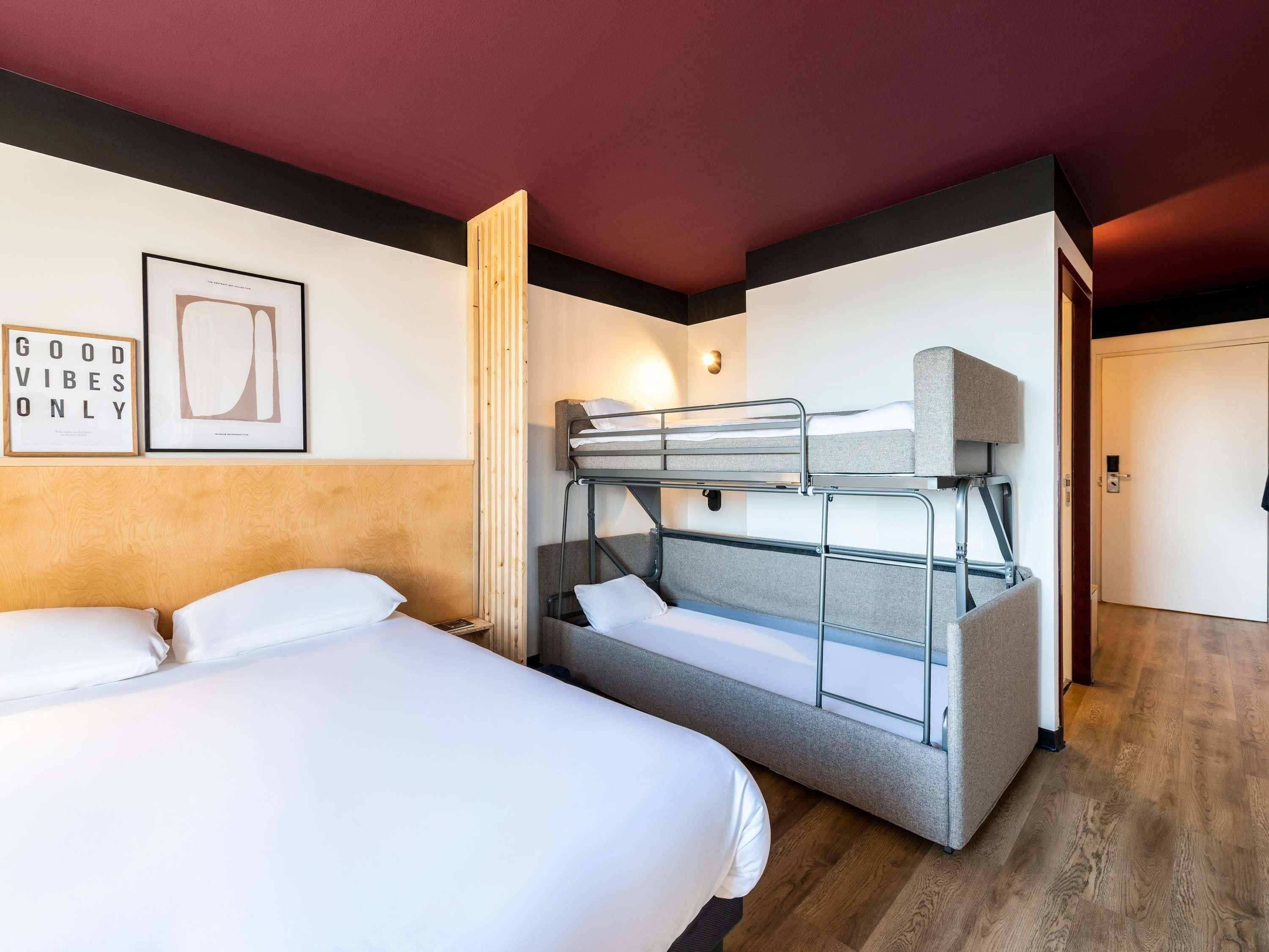 Habitación de hotel con literas, una cama individual, un cuadro enmarcado y una puerta.
