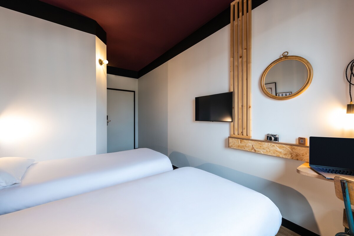 A hotel room with two beds, a wooden desk with a laptop, a TV, and a mirror.