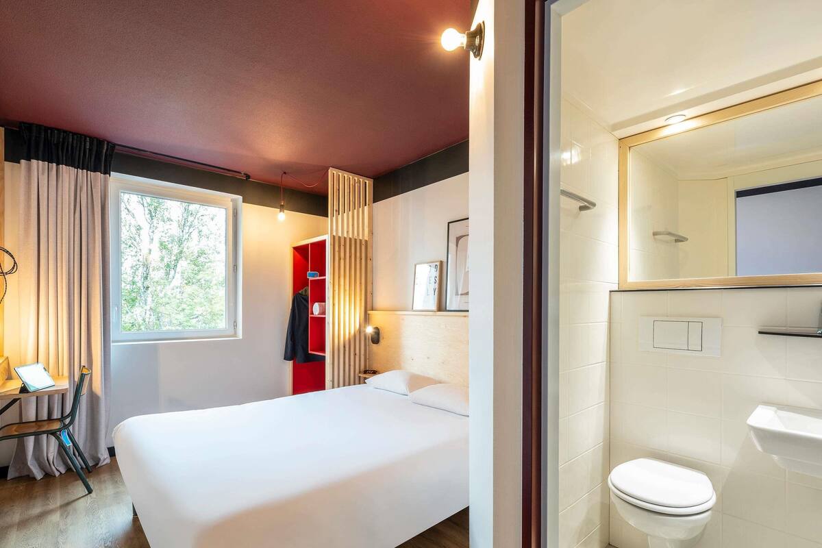 A modern bedroom with a large bed, a red wardrobe, and a bathroom with a white toilet and sink.