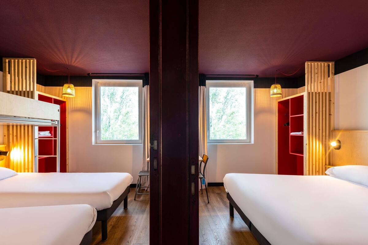 A mirrored room with two beds, wooden floors, and a window with a view of trees.