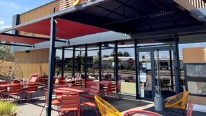 An outdoor seating area with red tables and chairs, a covered section with a 'greet' sign, and a view of the street through glass doors. - Greet Hotel Bourg-en-Bresse Sud Montagnat (Montagnat)