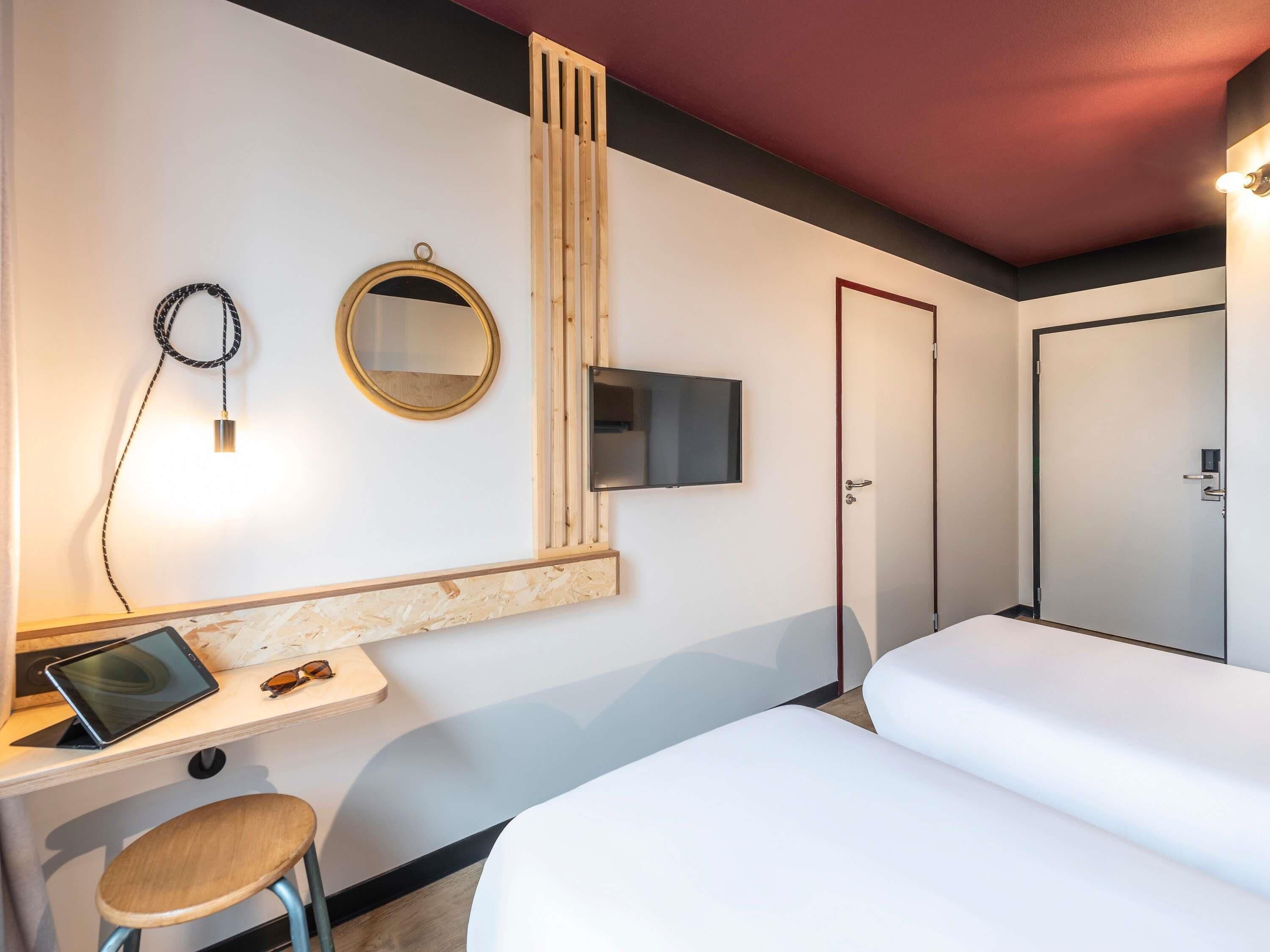 Una camera d'albergo con una scrivania, due letti, una televisione, uno specchio e una porta.