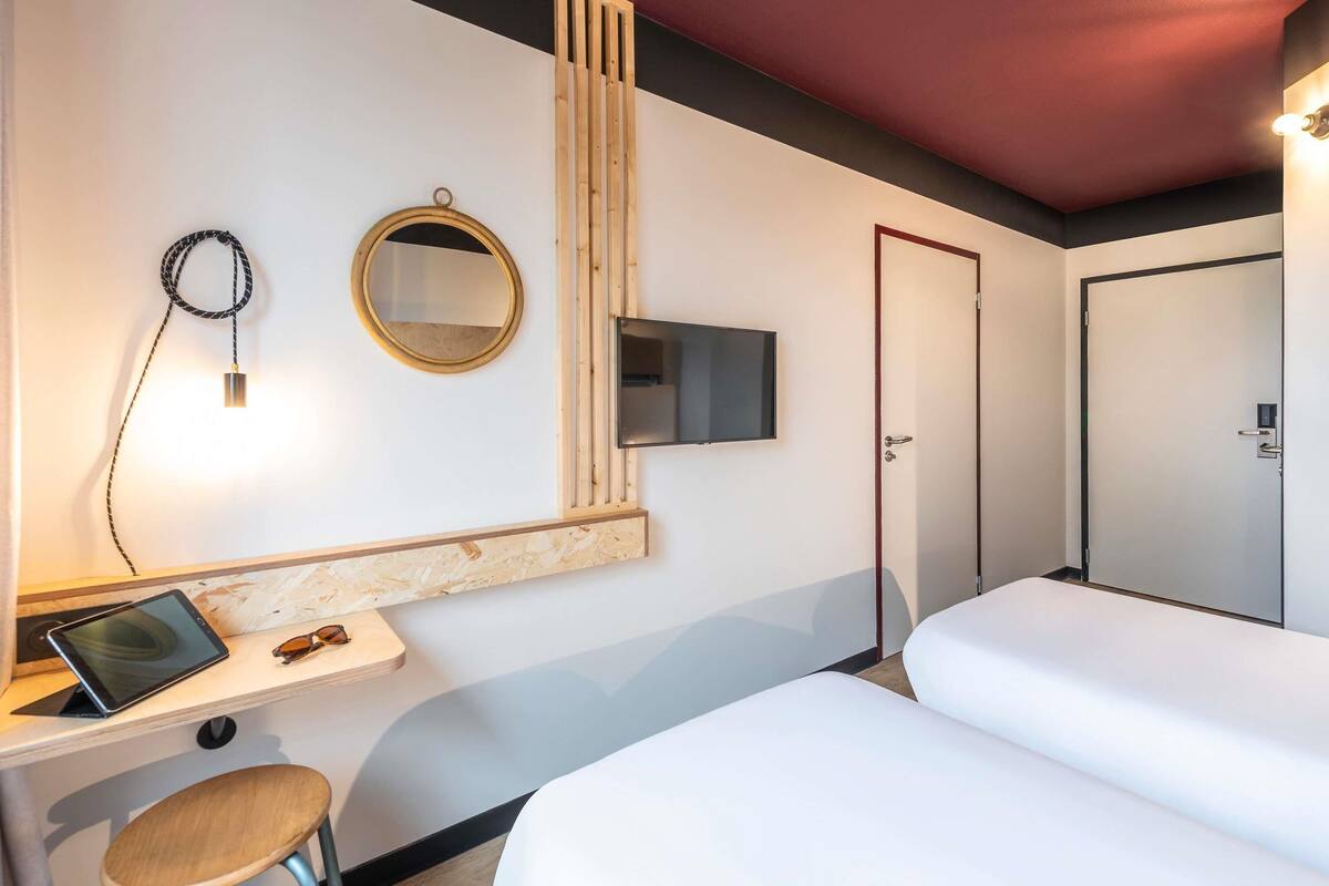 A hotel room with a desk, two beds, a TV, a mirror, and a door.