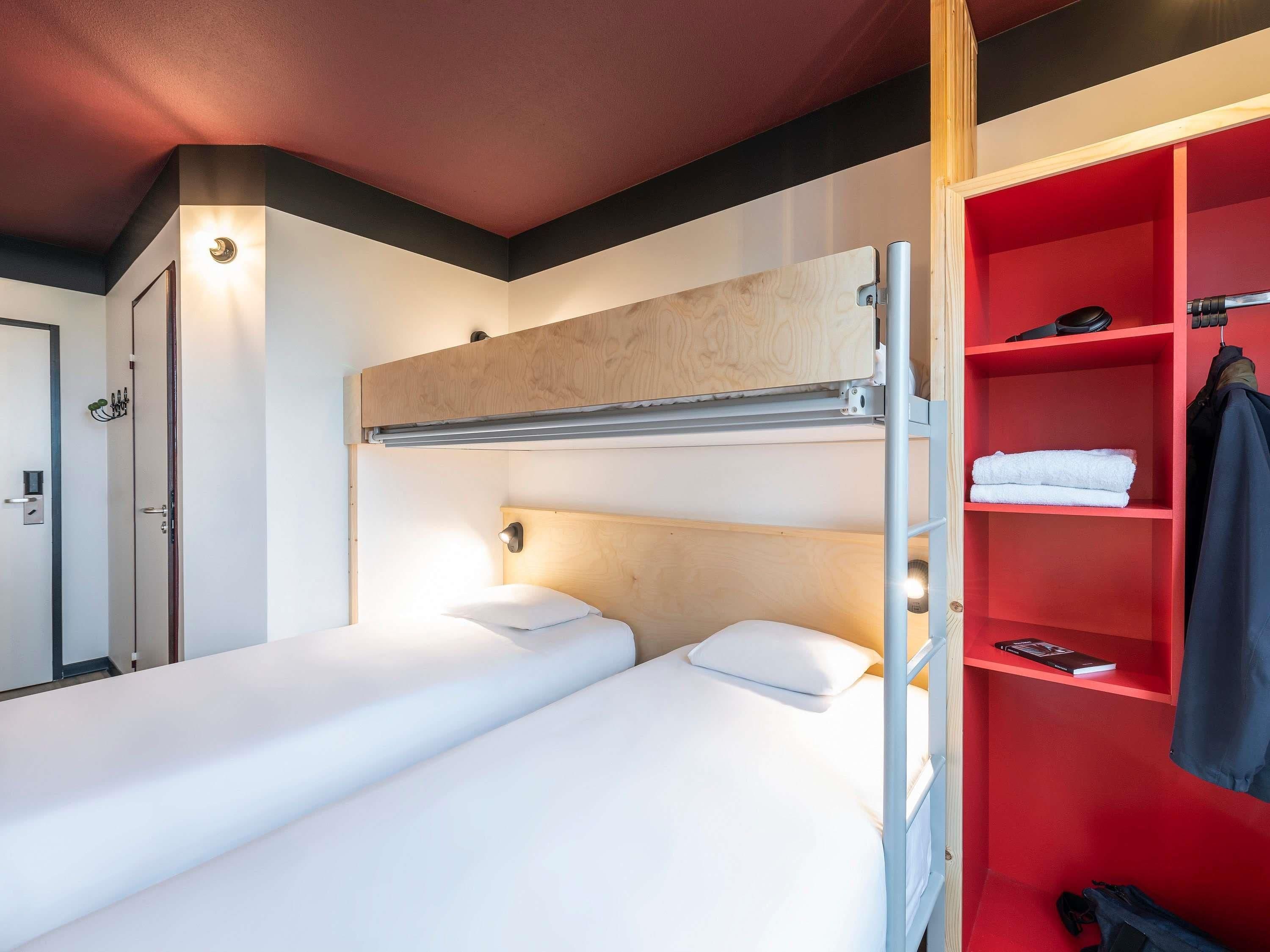 A hotel room with a bunk bed, a red wardrobe, and a door with a handle.