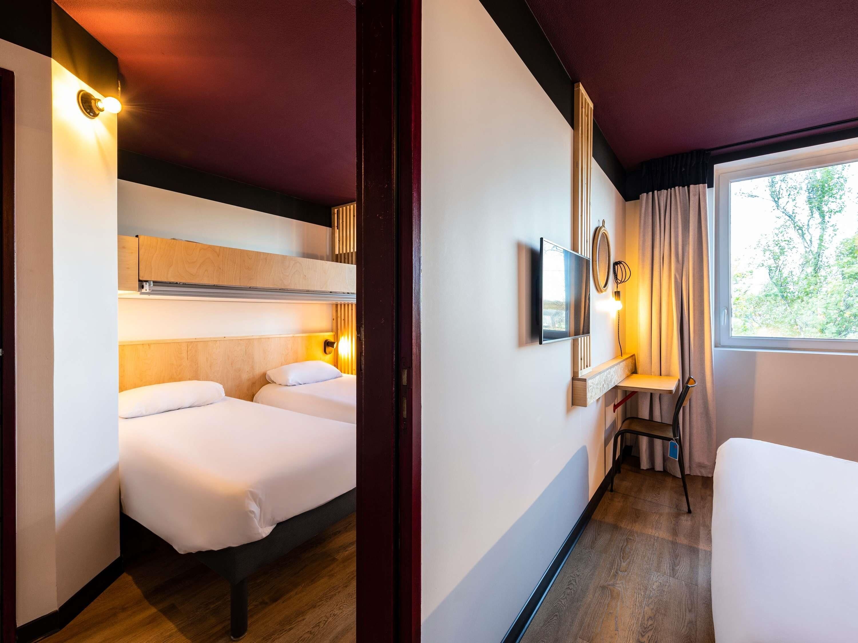 Una habitación de hotel con cama, escritorio, silla, televisor y ventana.
