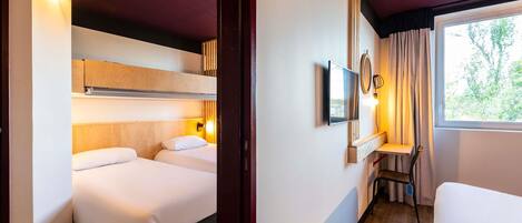 Una habitación de hotel con cama, escritorio, silla, televisor y ventana.
