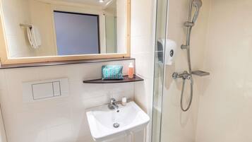 A modern bathroom with a glass-enclosed shower, a white sink, and a mirror above the sink.