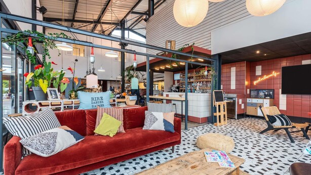 A modern interior with a red velvet sofa, wooden coffee table, and a bar area with shelves of bottles and glasses. - Greet Hotel Bourg-en-Bresse Sud Montagnat (Montagnat)