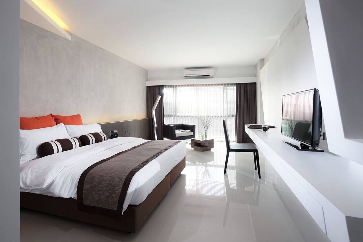 A modern hotel room with a large bed, a desk with a flat-screen TV, a chair, and a window with curtains.