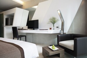 A modern hotel room with a bed, a desk with a computer, a chair, a coffee table, and a plant. - Nine Forty One Hotel (Bangkok)