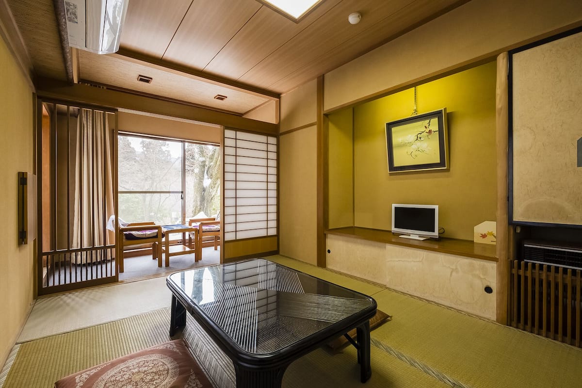 Una habitación japonesa tradicional con suelo de tatami, una mesa baja, un televisor y una puerta corredera que da a un jardín.
