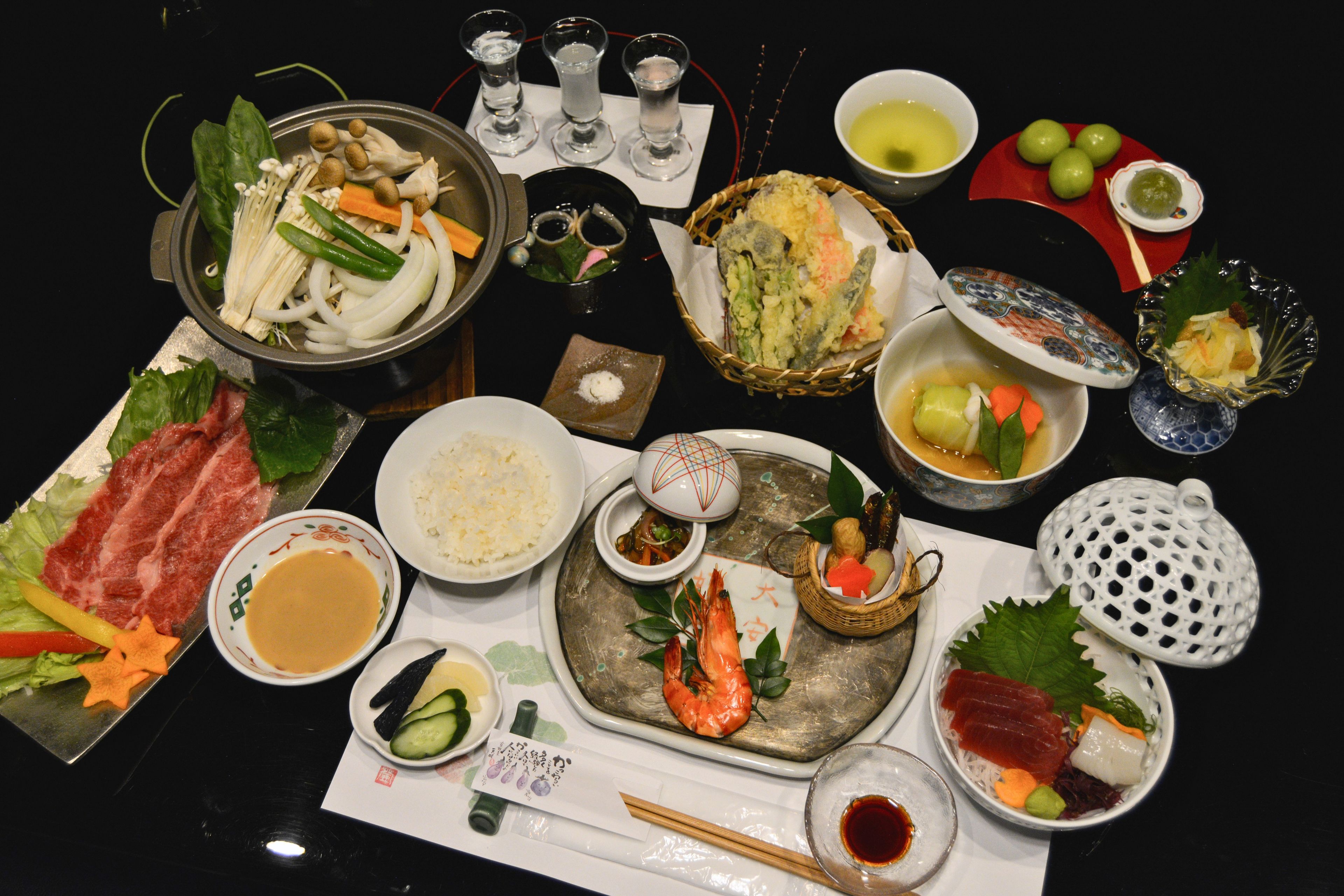 A variety of dishes including sashimi, vegetables, and rice, arranged on a table.