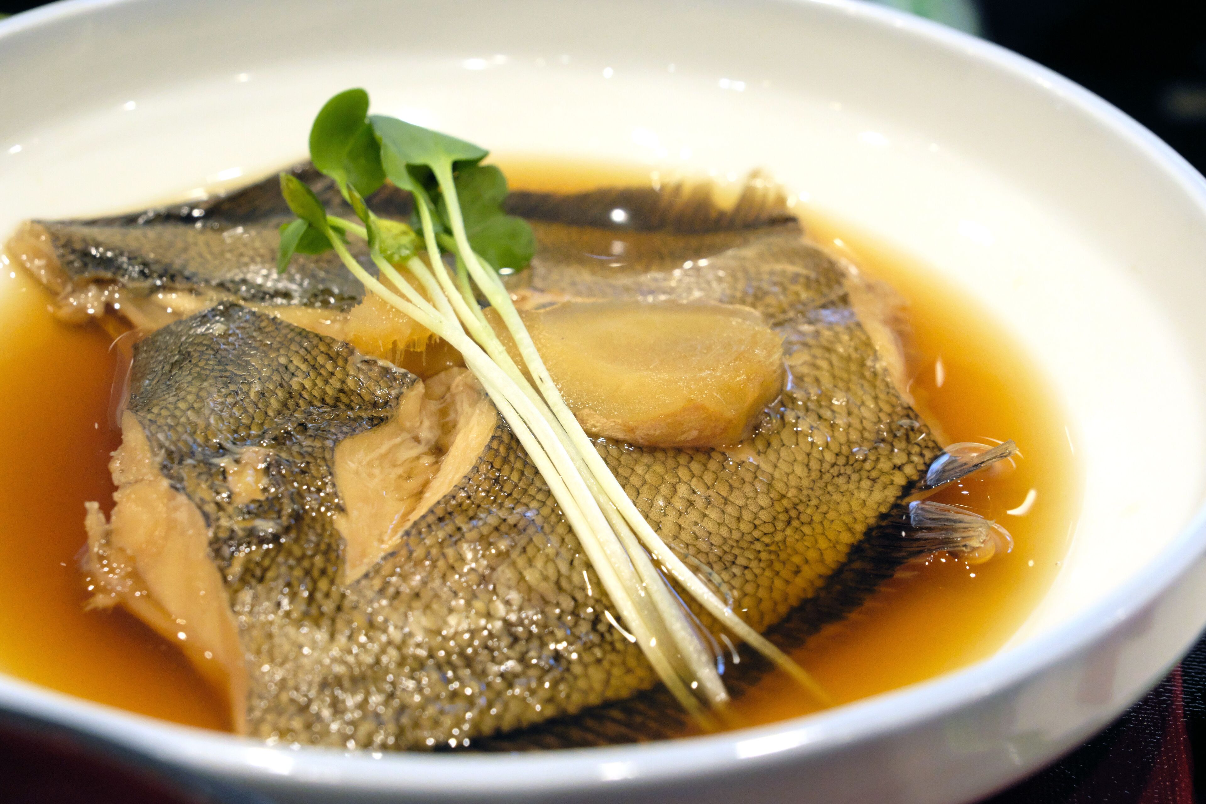 Un tazón de sopa de pescado con una guarnición de hojas verdes y tiras finas de verdura.