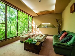Una habitación con un gran ventanal, un sofá verde, una mesa de centro de madera y una mesita con adornos.