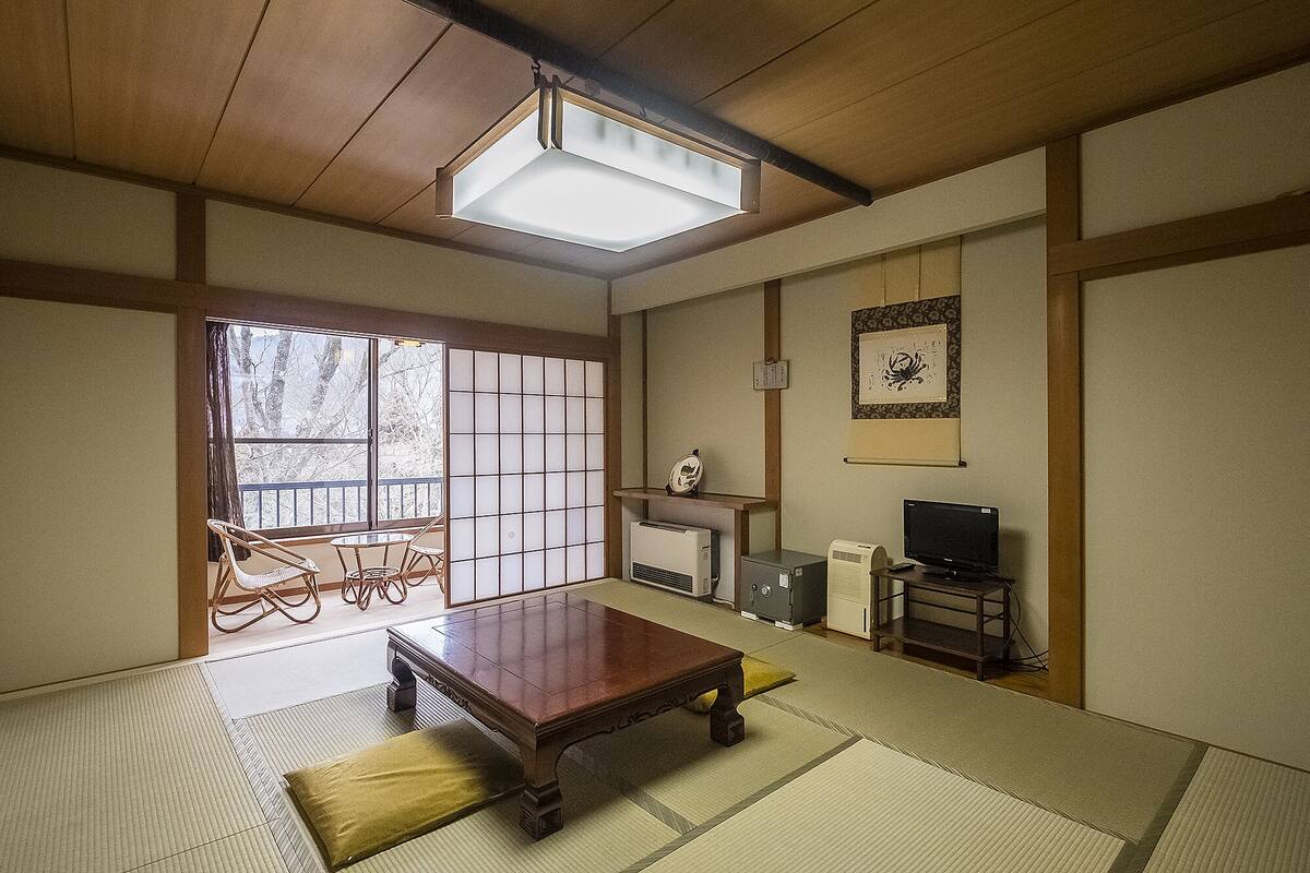 Una habitación japonesa tradicional con suelo de tatami, una mesa de madera baja, un sofá, un televisor y una chimenea.