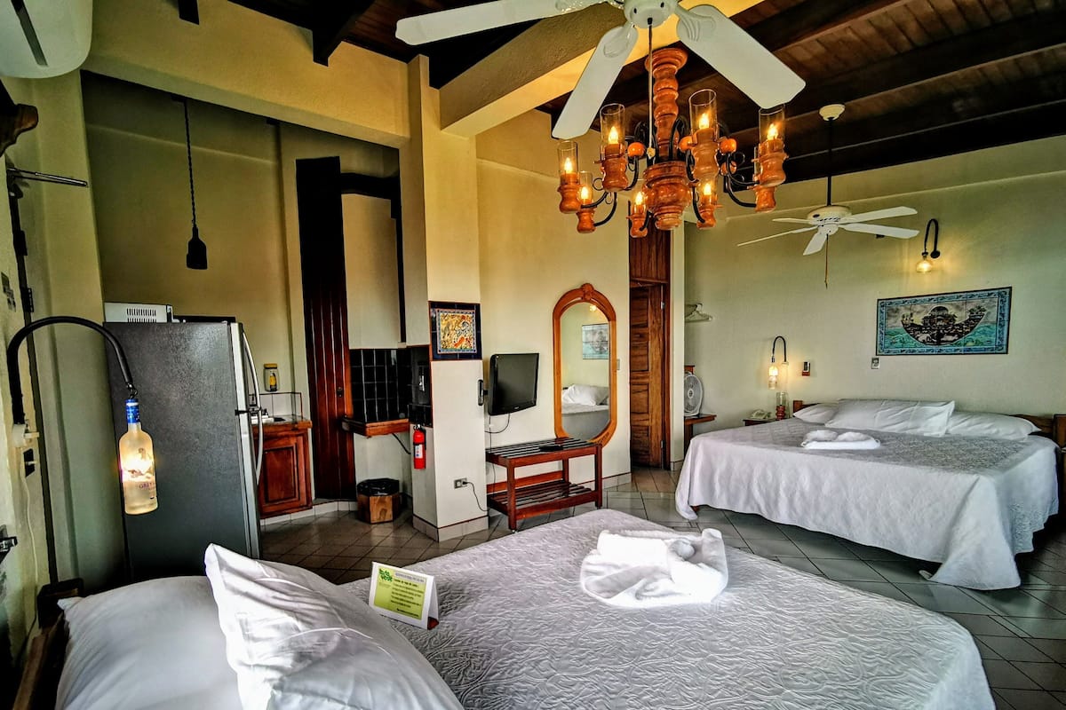 A hotel room with two beds, a ceiling fan, a chandelier, a refrigerator, a television, and a mirror.