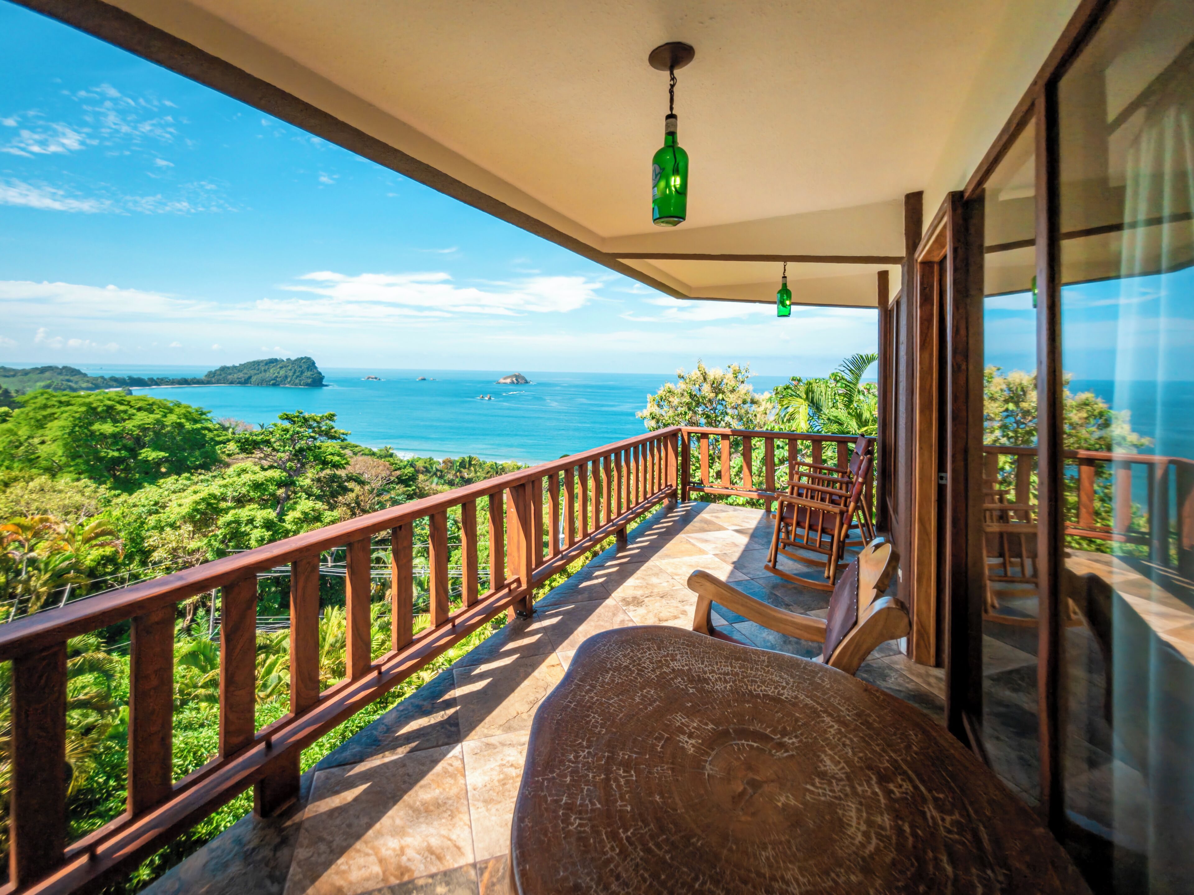 A balcony with a view of the ocean, wooden furniture, and a hanging light fixture.