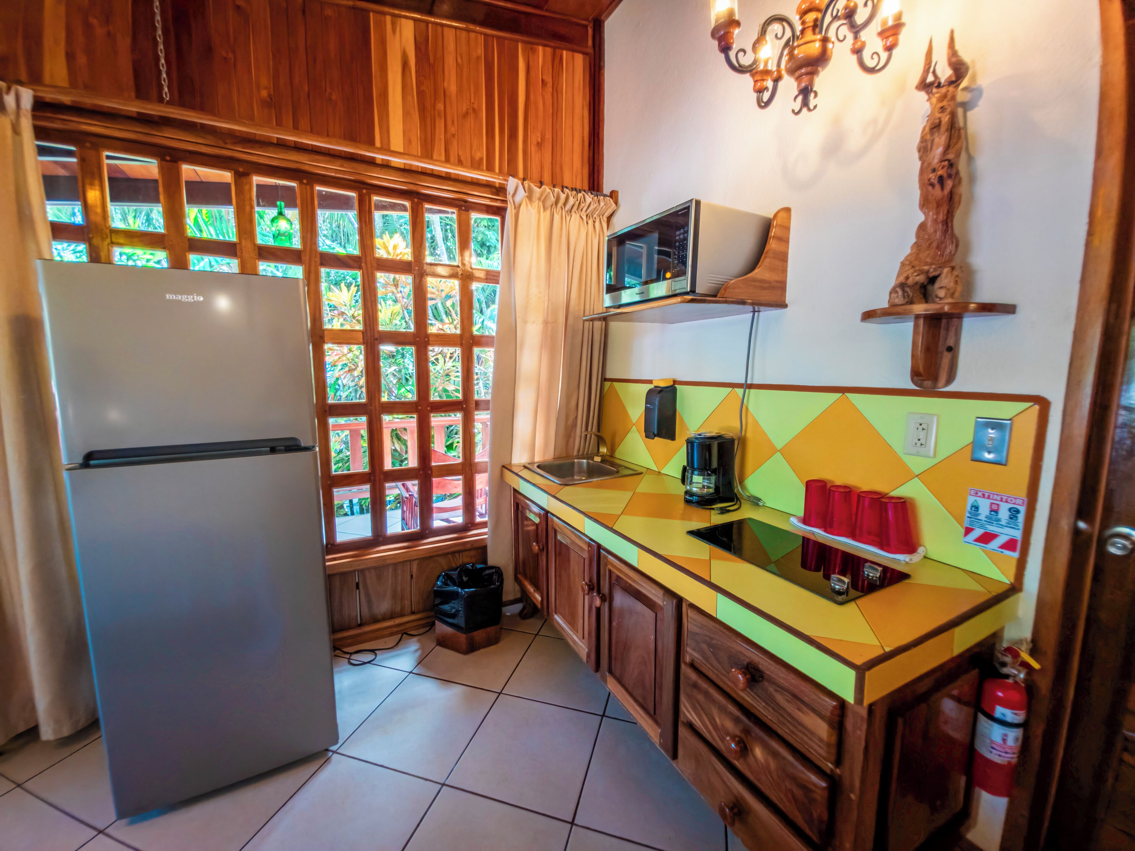 A kitchen with a refrigerator, a microwave, a coffee maker, and a window with a view of greenery.