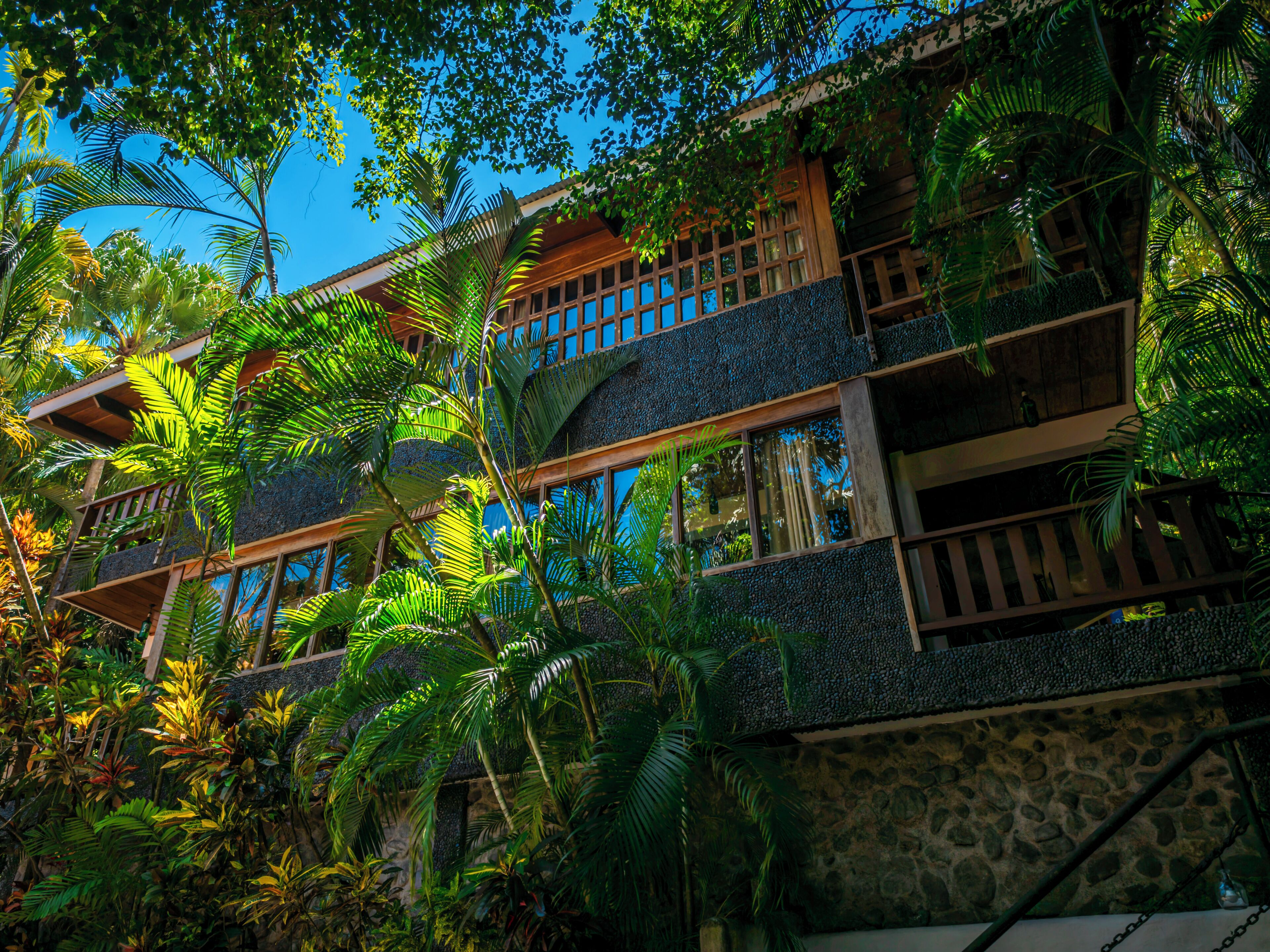 Un edificio de varios pisos con balcones, rodeado de exuberante vegetación tropical.