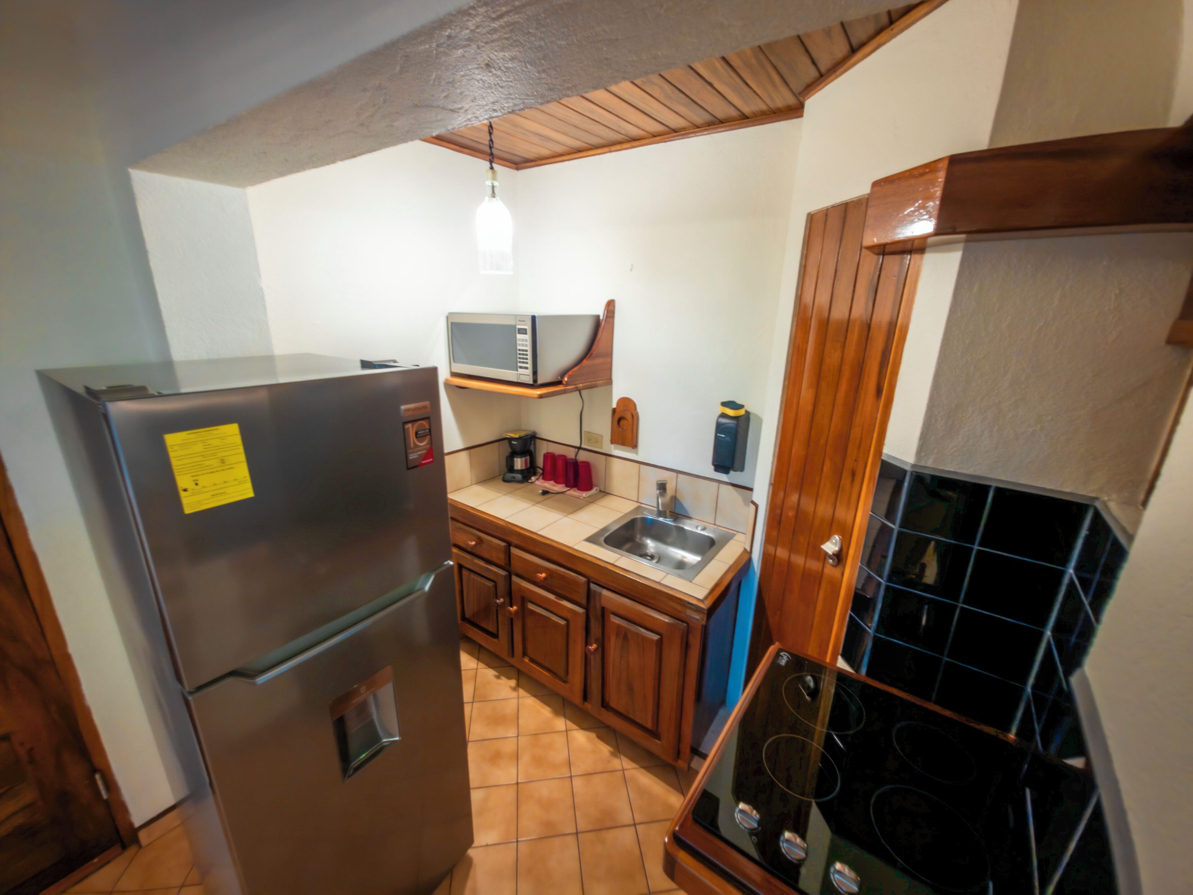Cocina compacta equipada con refrigerador, microondas, lavamanos y estufa.