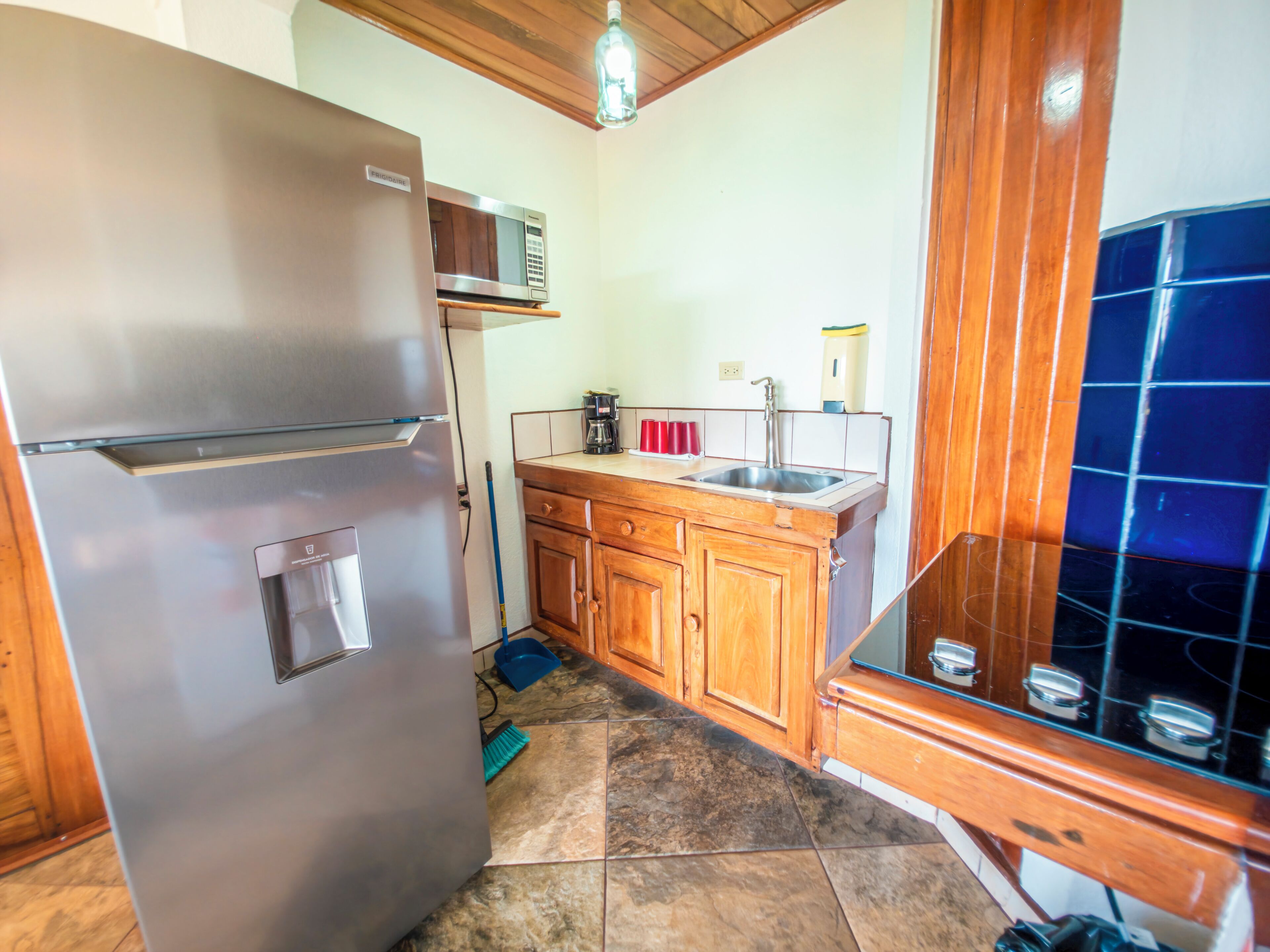 Una cocina con un refrigerador de acero inoxidable, armarios de madera, un microondas, un lavamanos y un salpicadero de azulejos azules.