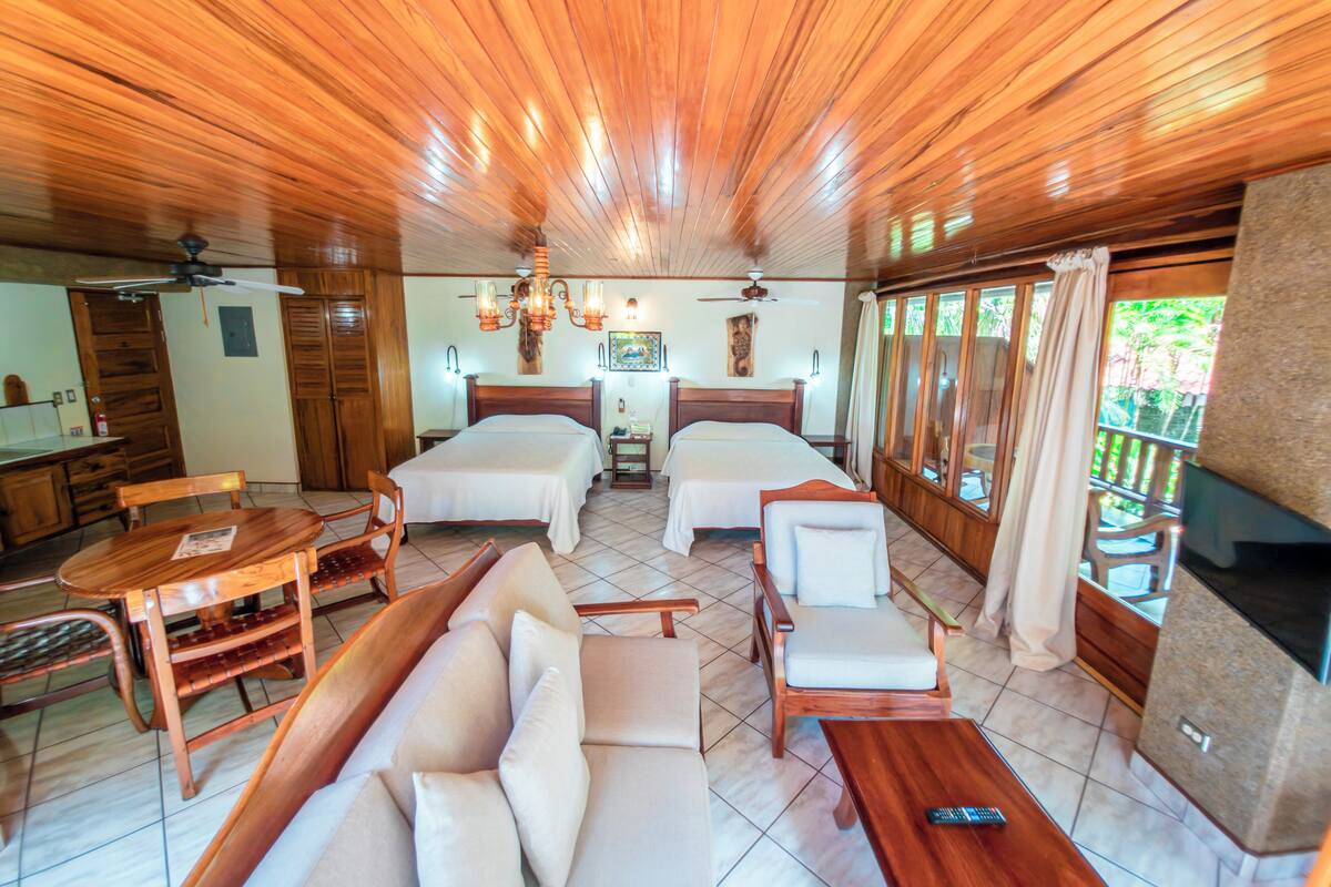 A hotel room with two beds, a sofa, a dining table, and a TV.