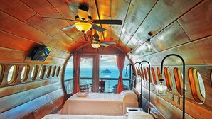 Een knus huisje met een bed, een plafondventilator en uitzicht op de oceaan.