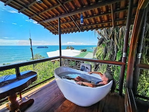 A room with a large bathtub, a wooden deck, and a view of the ocean.