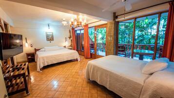 Habitación de hotel con dos camas, televisión, ventilador de techo y balcón con vistas a zonas verdes.