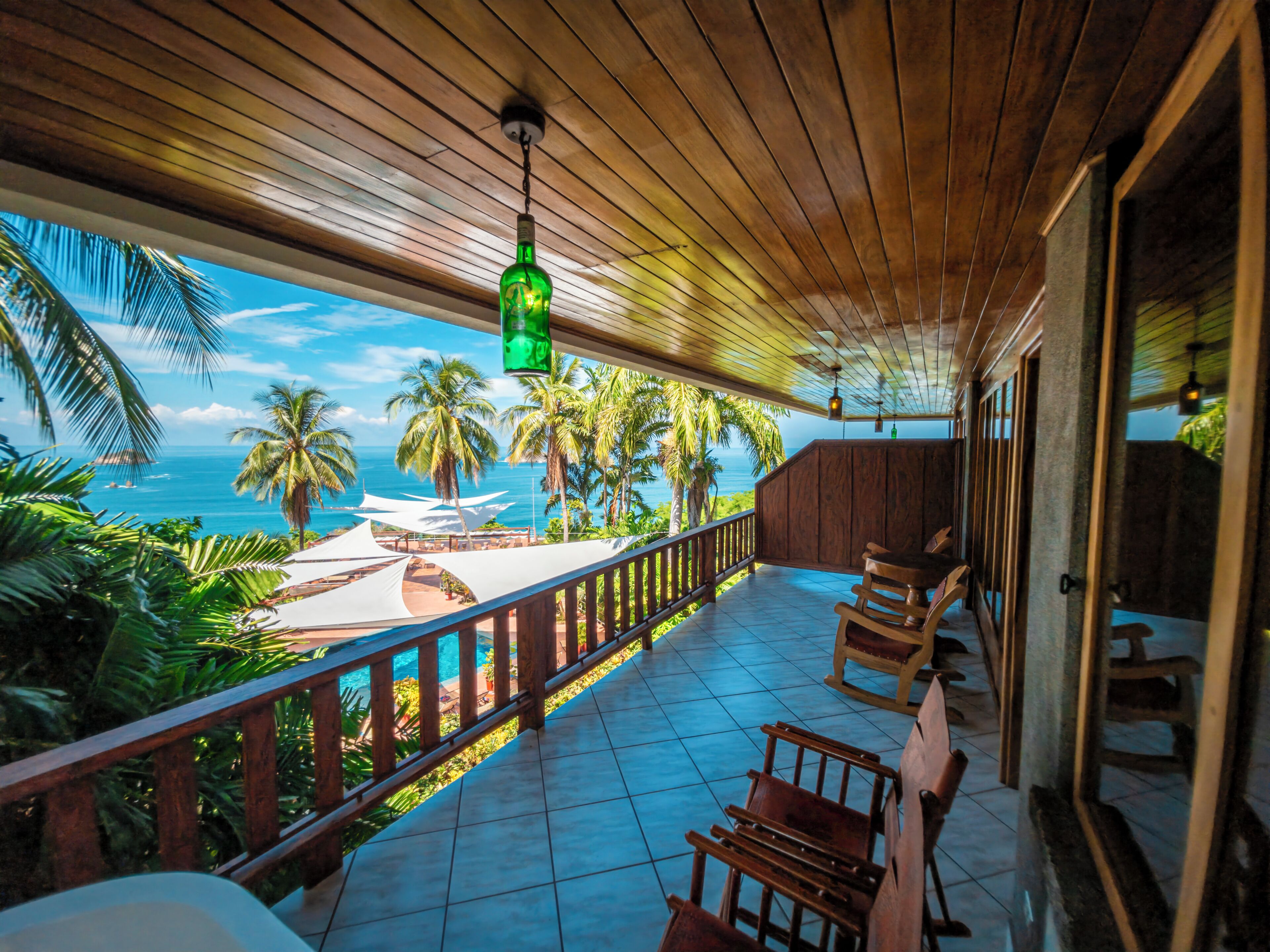 A wooden deck with a view of the ocean, palm trees, and a tiled floor.