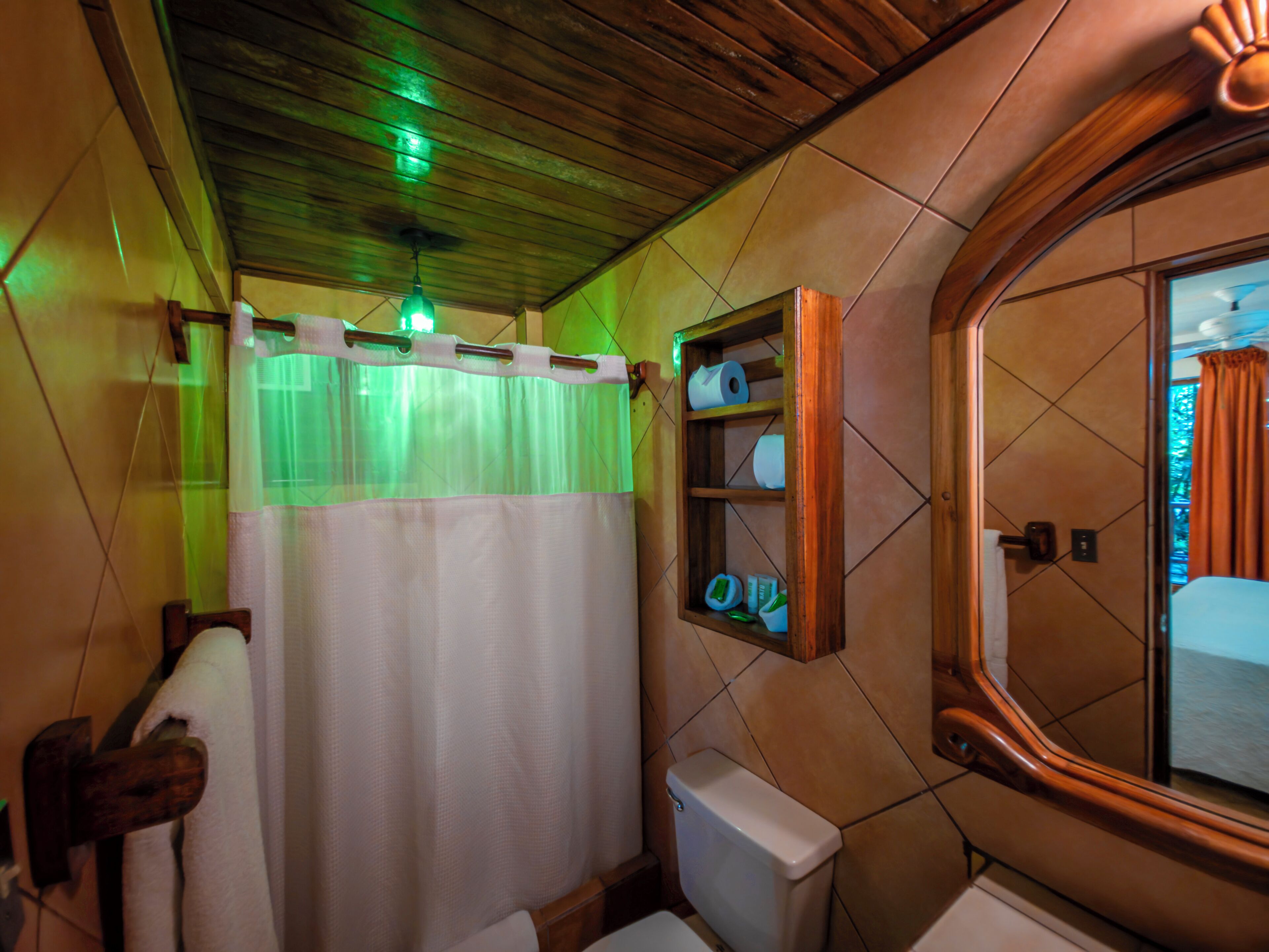 Une salle de bain avec un plafond en bois, des toilettes, un rideau de douche, un porte-serviettes et un miroir.