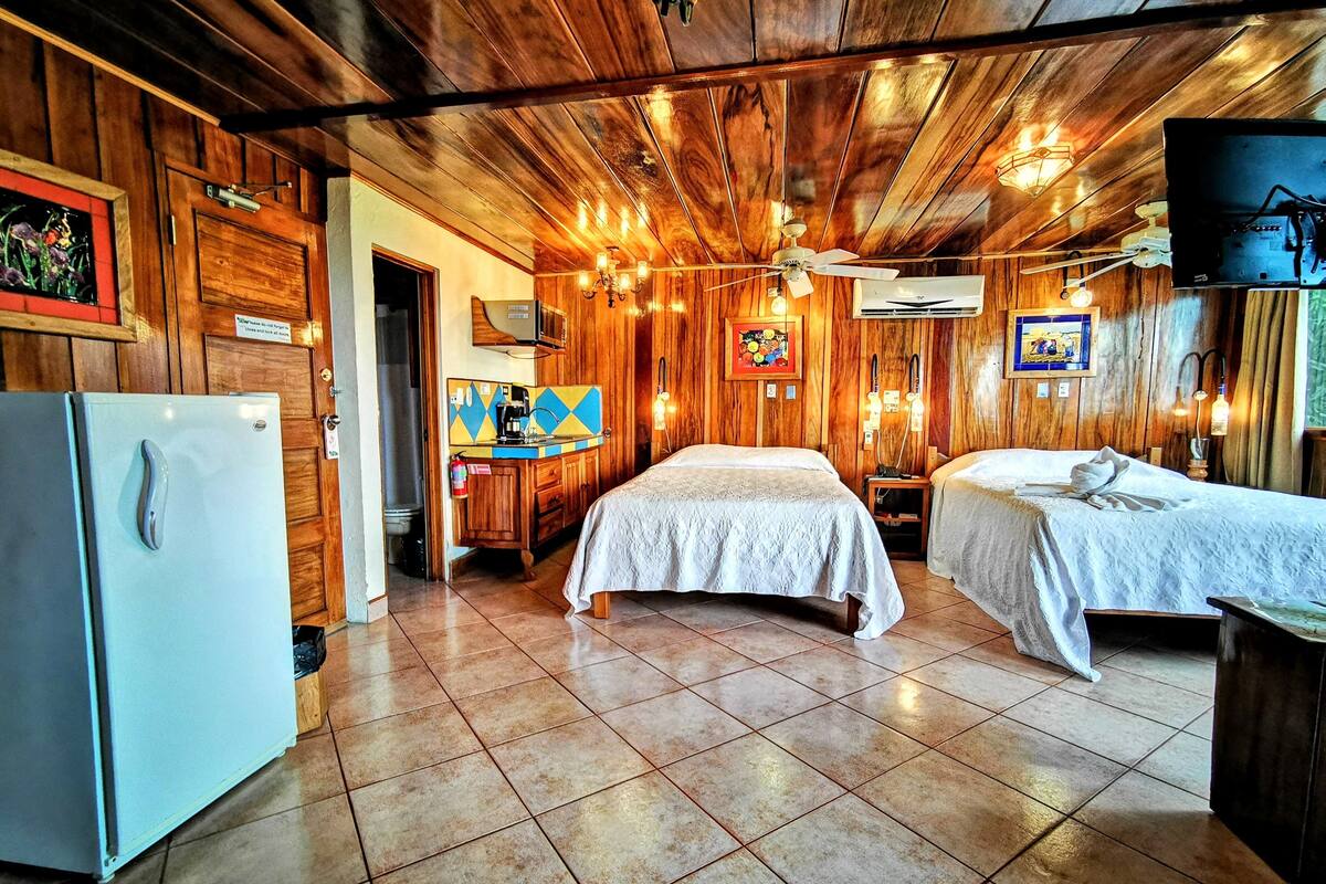 A room with wooden walls and ceiling, two beds, a refrigerator, a sink, and a television.