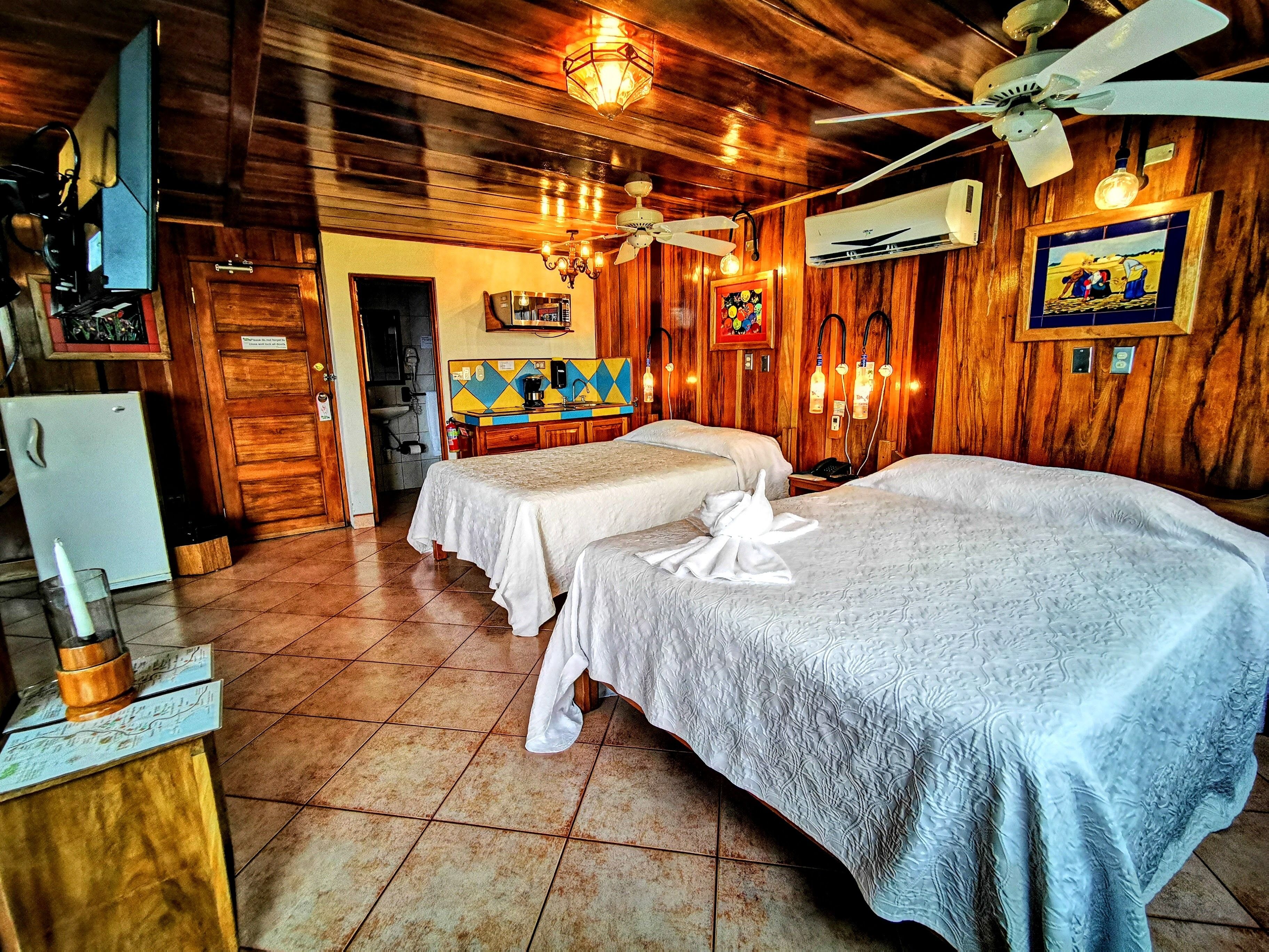 Una camera d'albergo con due letti, angolo cottura, ventilatore a soffitto e pareti in legno.