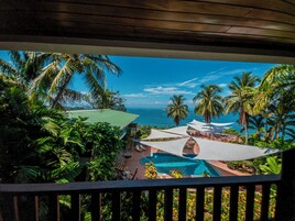 Zona de piscina con sombrillas, palmeras y vista al océano.