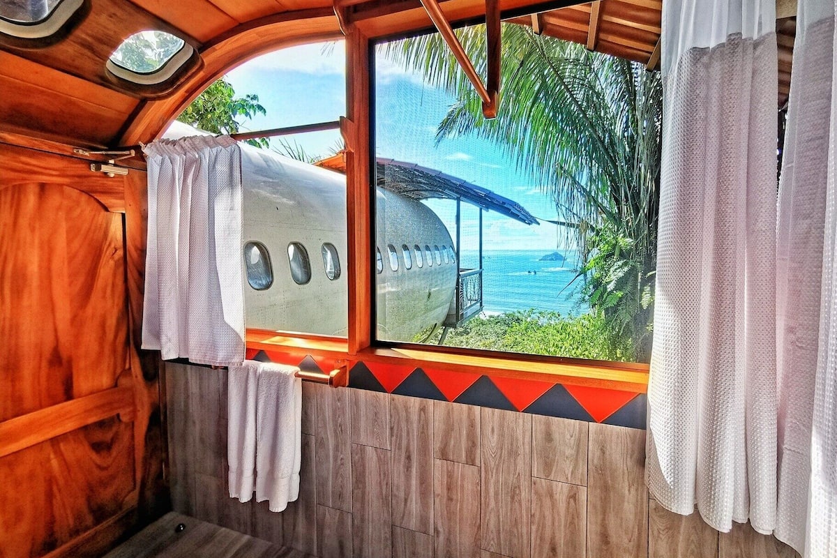 A cabin with a window view of a beach and palm trees.