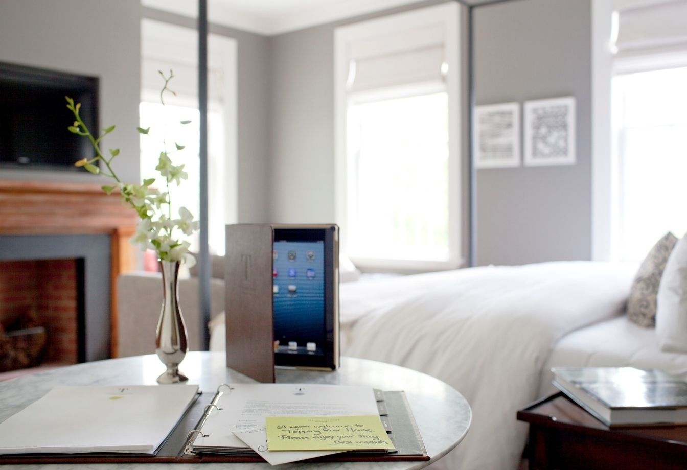 Habitación de hotel con cama, escritorio con computadora portátil, florero con flores y chimenea.