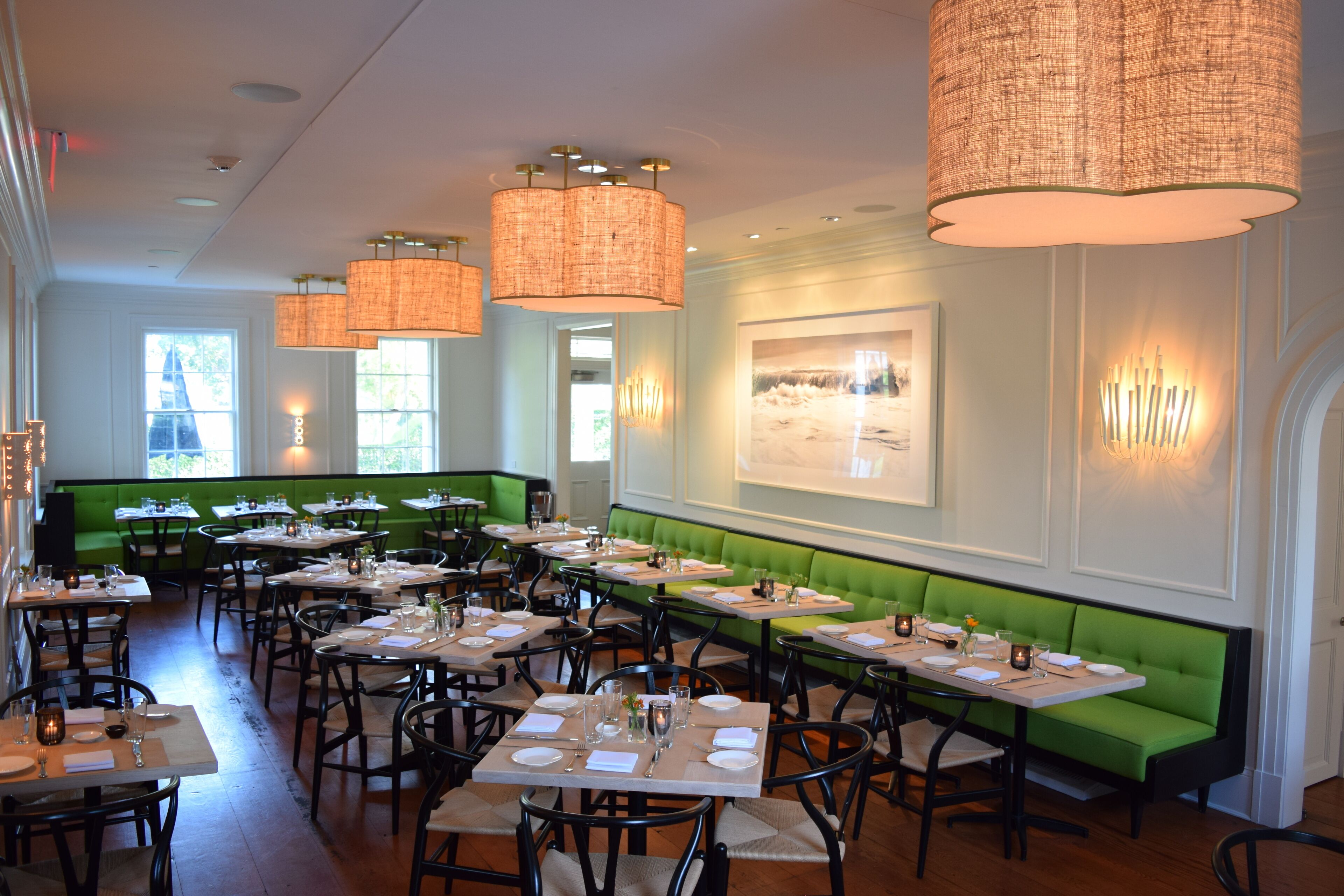 A restaurant with multiple tables and green booths, featuring wicker chandeliers and framed artwork on the walls.