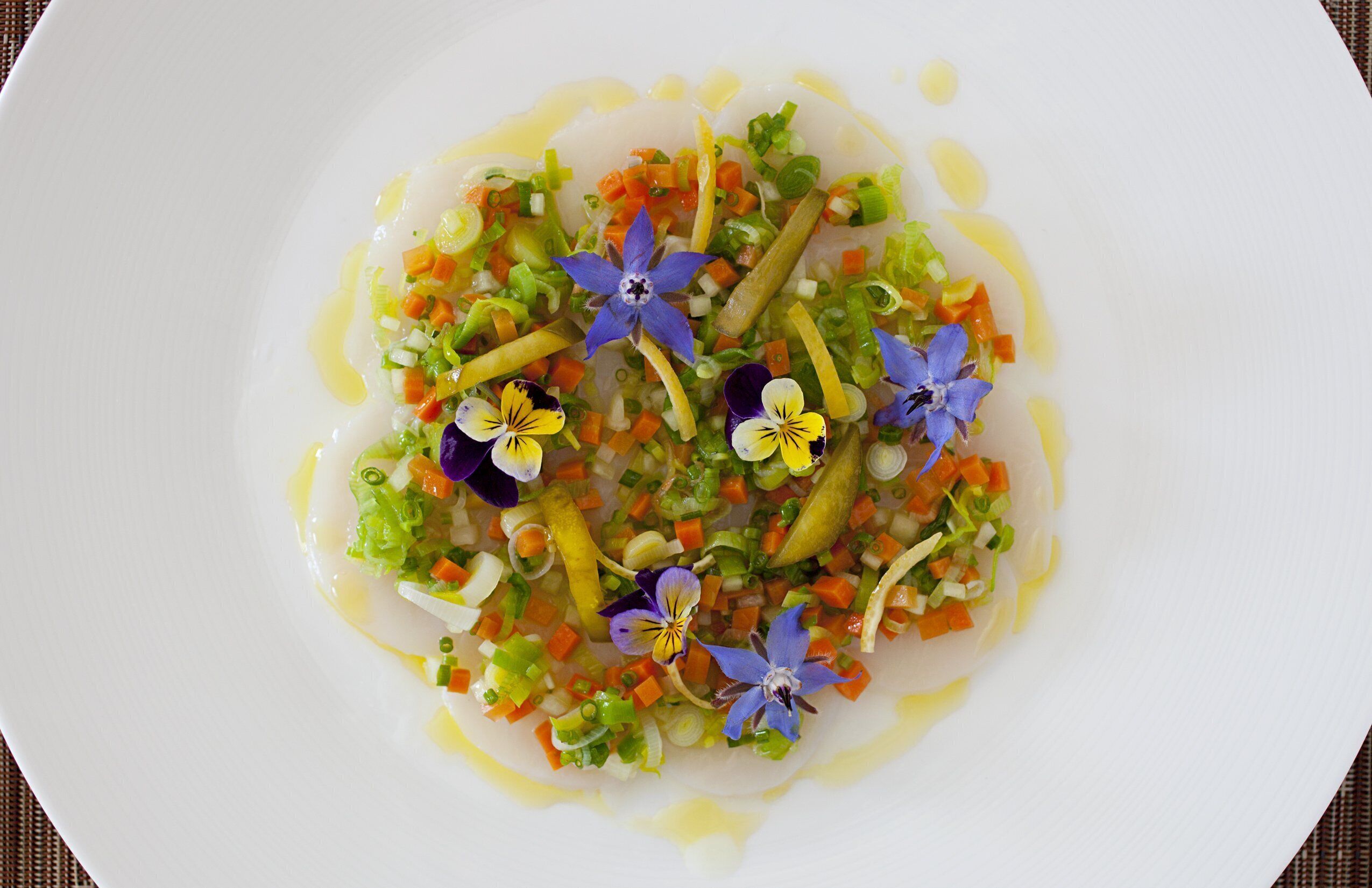 En vit tallrik med en färgstark sallad bestående av grönsaker och blommor.