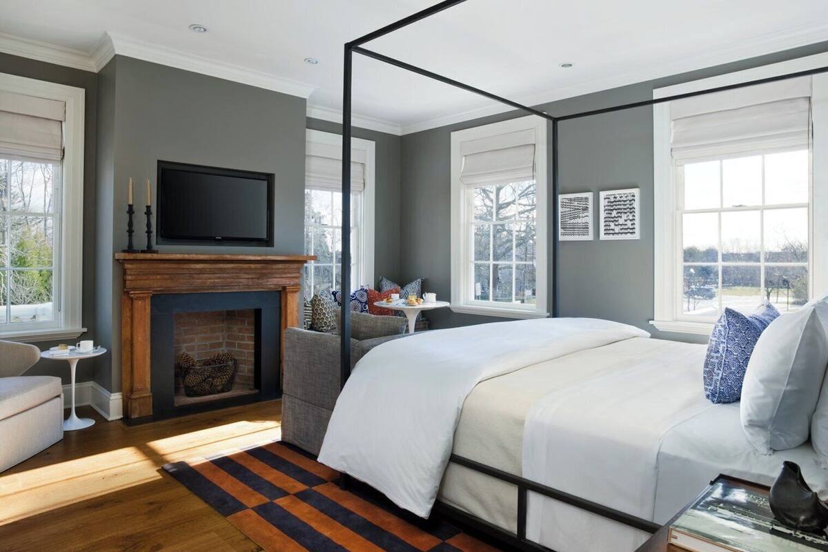 A bedroom with a four-poster bed, a fireplace, a television, and large windows.