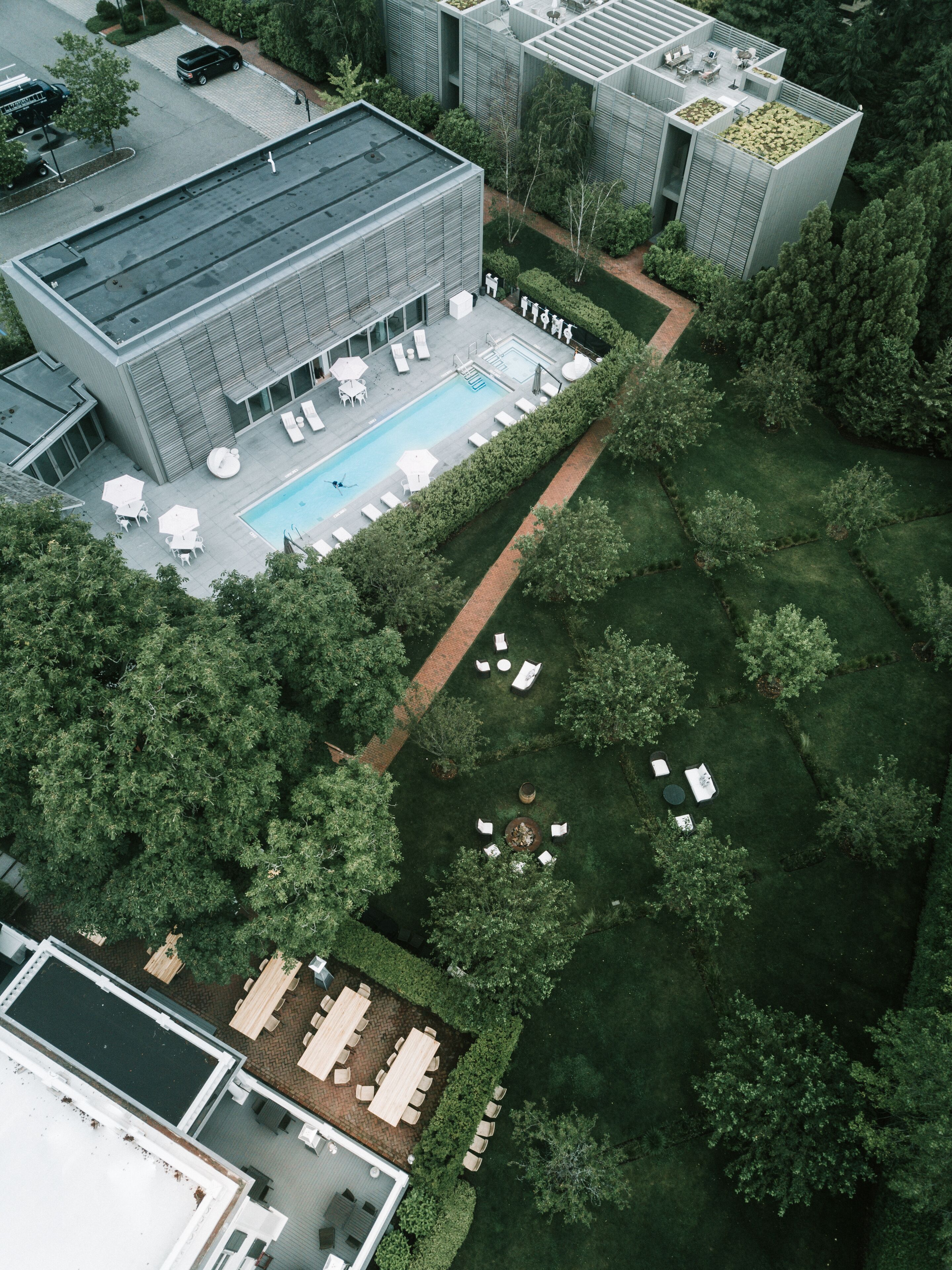 An aerial view of a modern building with a swimming pool, outdoor seating, and a well-maintained garden.
