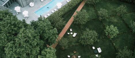 An aerial view of a modern building with a swimming pool, outdoor seating, and a well-maintained garden.