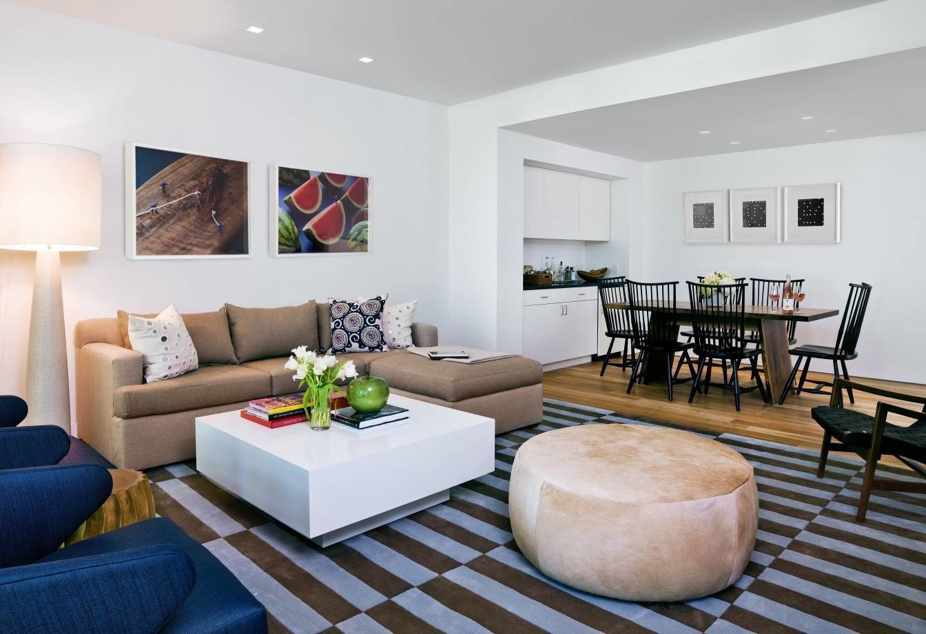 Un salon moderne comprenant un canapé, une table basse, un pouf et un coin repas avec des chaises et une table.
