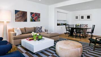 A modern living room with a sofa, coffee table, ottoman, and a dining area with chairs and a table.