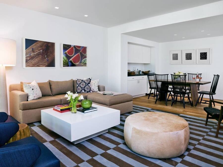 A modern living room with a sofa, coffee table, ottoman, and a dining area with chairs and a table.