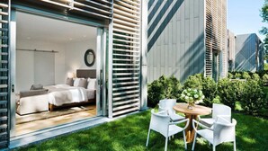 A modern hotel room with a bed, bedside table, and a view of the garden. - Topping Rose House (Bridgehampton)