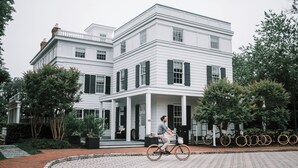 A large, white, two-story building with a covered porch and a bicycle parked in front. - Topping Rose House (Bridgehampton)