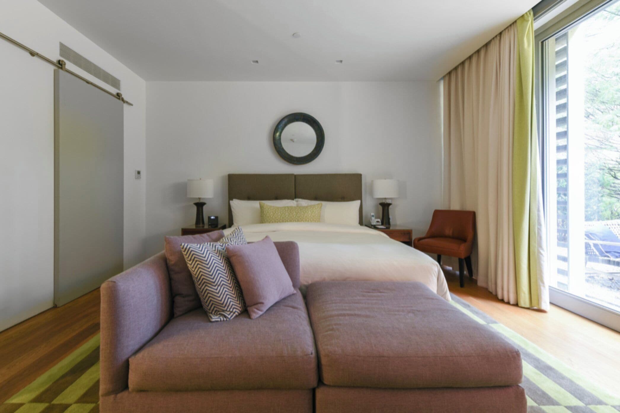 Una habitación de hotel moderna con una cama grande, un sofá, una silla y un ventanal con cortinas.