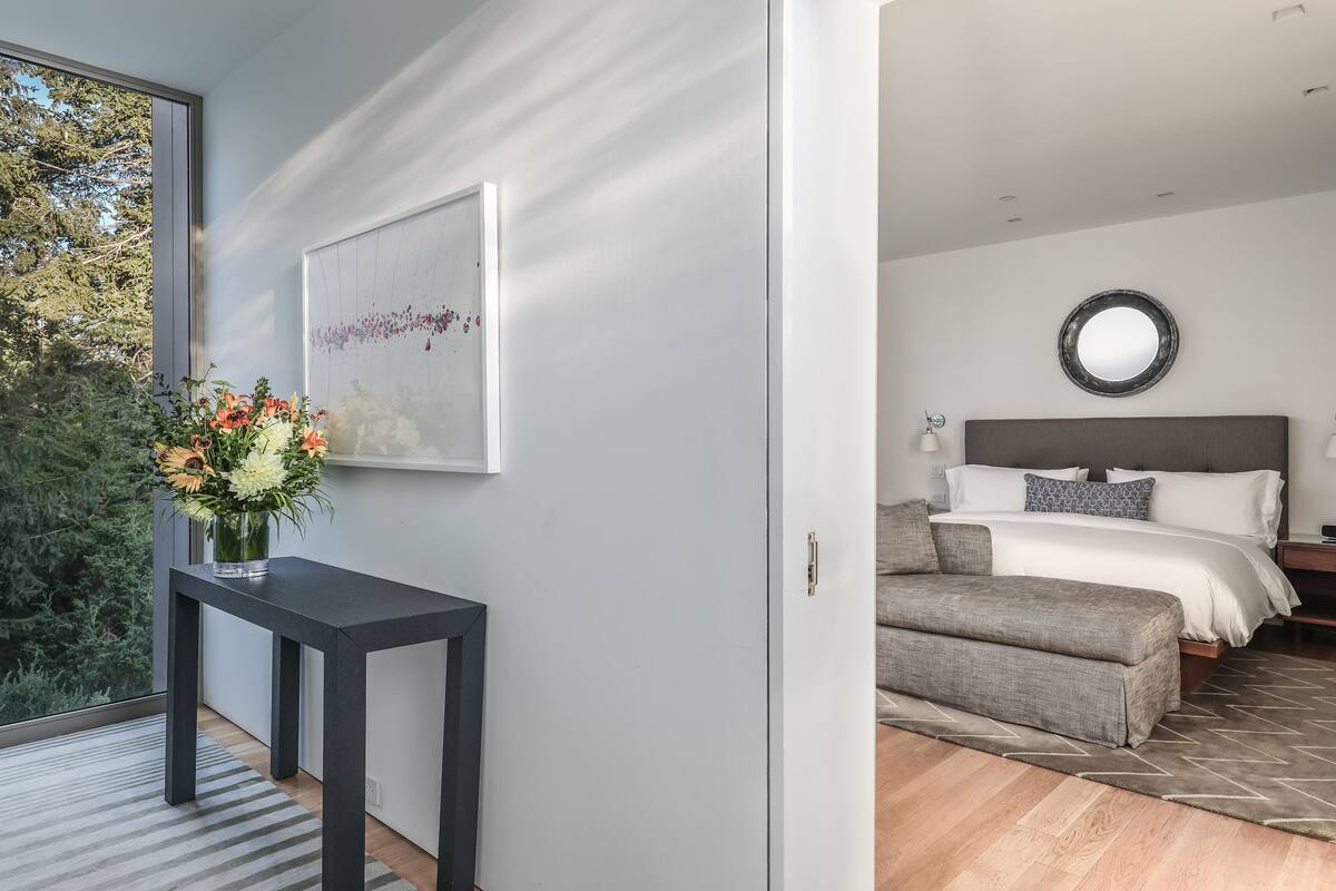 A modern bedroom with a bed, bedside table, and a large window with a view of trees.