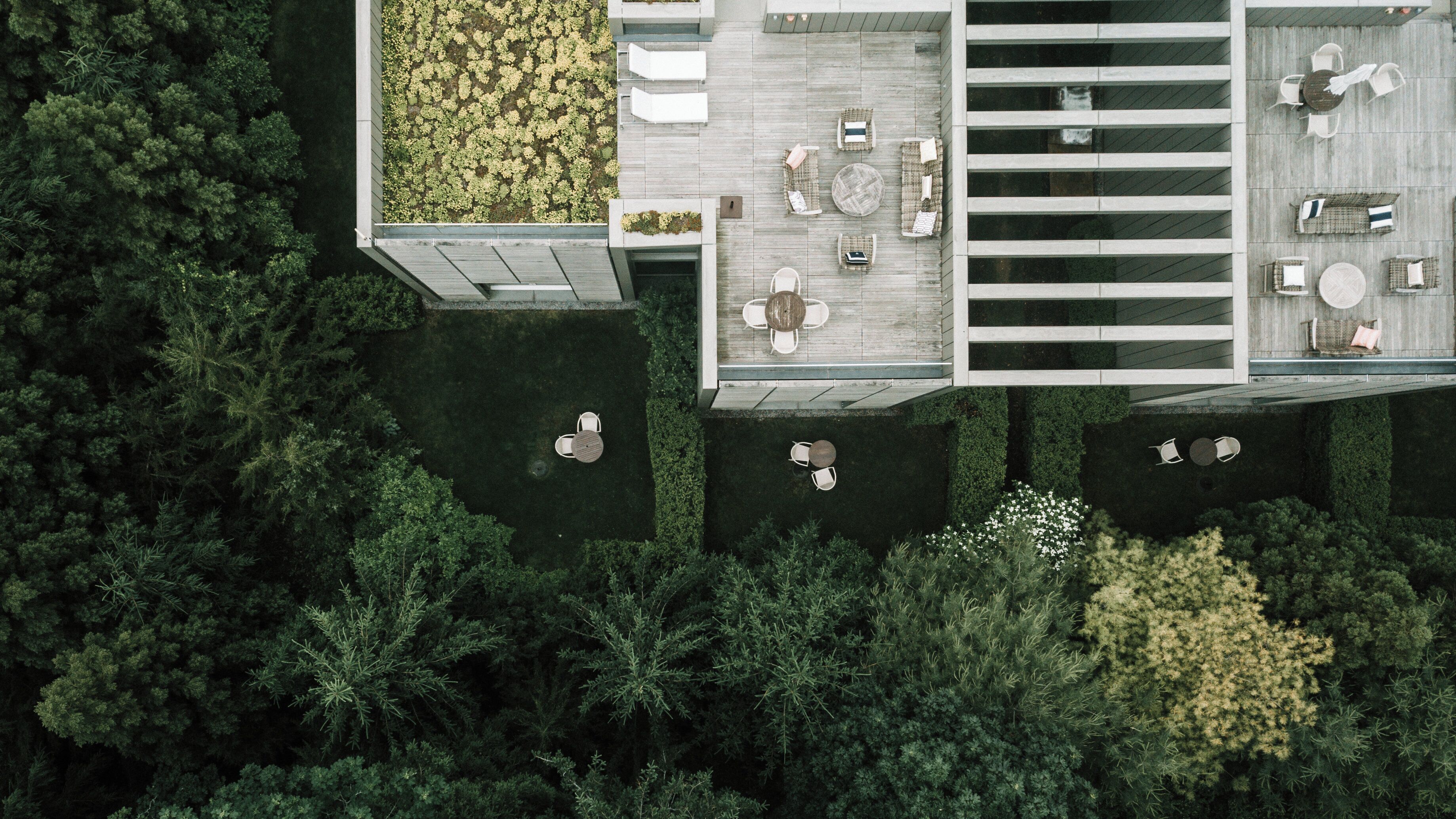 An aerial view of a modern outdoor patio with multiple seating areas, surrounded by dense greenery.