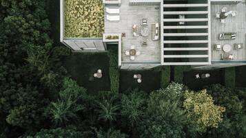 An aerial view of a modern outdoor patio with multiple seating areas, surrounded by dense greenery.
